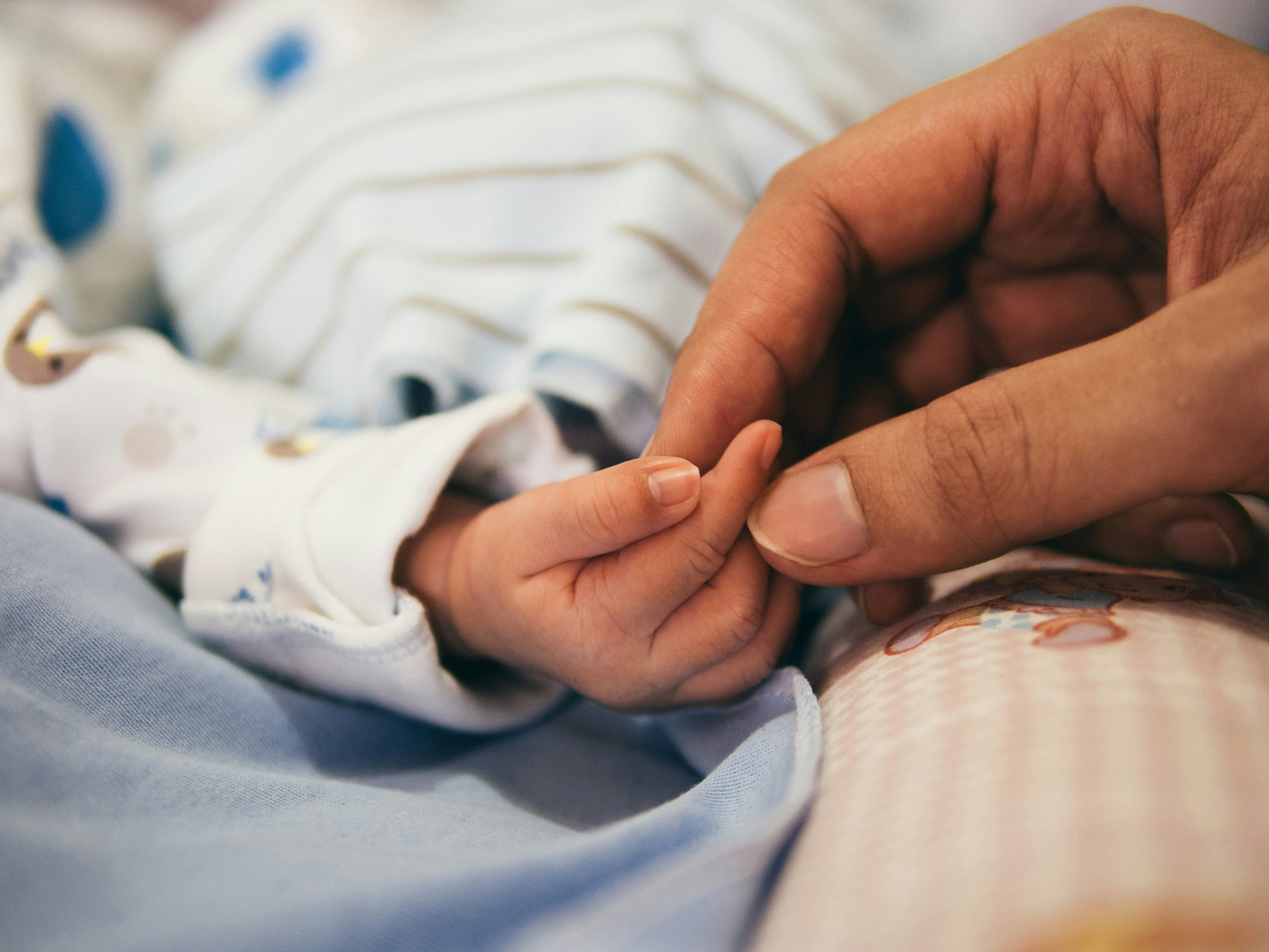 A newborn's hand holding an adult's finger.